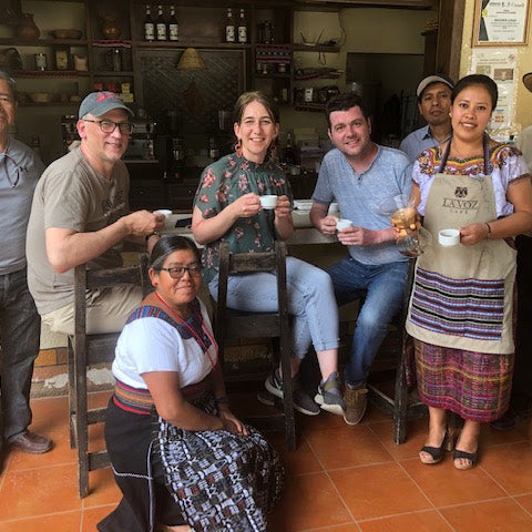 Group of people posing together in a rustic setting with a woman in traditional attire holding a cup.