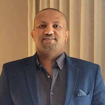 Man wearing a blue suit with a patterned shirt against a beige curtain background